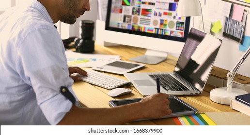 Porträt von jungen Designern, die im Grafikstudio vor Laptop und Computer sitzen, während sie online arbeiten.