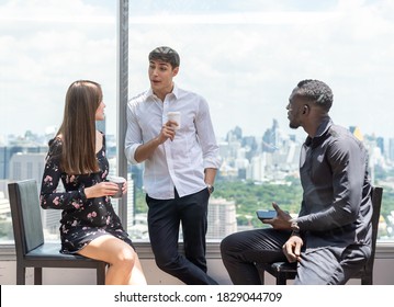 Portrait Of Young Diverse Creative Business Team Standing, Sitting And Talking Together Over Cityscape Blur Background. Group Of Young Business People Take A Break Using Mobile Phone, Drinking Coffee