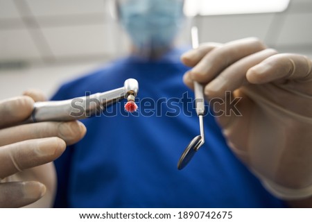 Portrait of a young doctor dentist holding tools and instruments while standing at work. View from the first patient's face. People, medicine, stomatology and health care concept