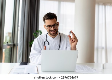 Portrait Of Young Doctor Talking To Online Patient On Laptop Screen Sitting At Clinic Office Desk Giving Online Consultation For Domestic Health Treatment. Telemedicine Remote Medical Appointment