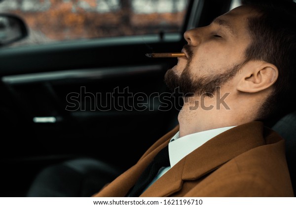 Portrait of a young\
drunk guy sleeping with a cigarette while driving a car. Close-up.\
In a warm, creative\
tone