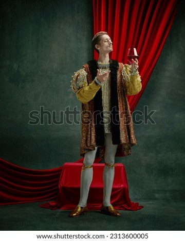 Portrait of young duke, prince, royal person in vintage costume raising glass of red wine against dark green, vintage background. Concept of comparison of eras, history, renaissance art, remake