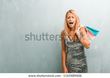 Portrait of young elegant blonde woman screaming angry, expression of madness and mental instability, open mouth and half-opened eyes, madness concept. Holding shopping bag.