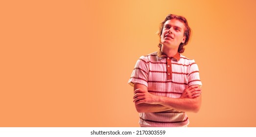 Portrait of young emotive man with thoughtful dreamy look, posing, looking upwards isolated on orange studio background in neon light. Concept of youth, fashion, lifestyle, emotions. Copy space for ad - Shutterstock ID 2170303559