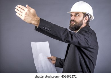 Portrait of young engineer holding plan drawings and explaining something isolated on gray background