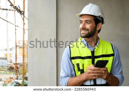 portrait of young engineer in vest with white helmet standing on construction site, smiling and holding smartphone for worker, internet, social media Stock fotó © 