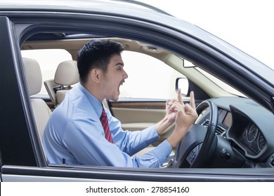 Portrait of young entrepreneur looks angry in the car while showing two middle fingers and shouting