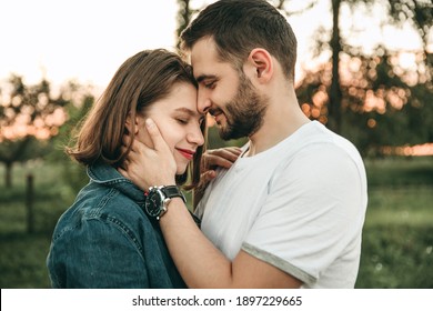 Portrait of young european couple man and woman hugging in green park at sunset. Girl in a blue denim shirt, a guy in a white T-shirt. Happy relationship, love, date, hand on face, passion. - Powered by Shutterstock