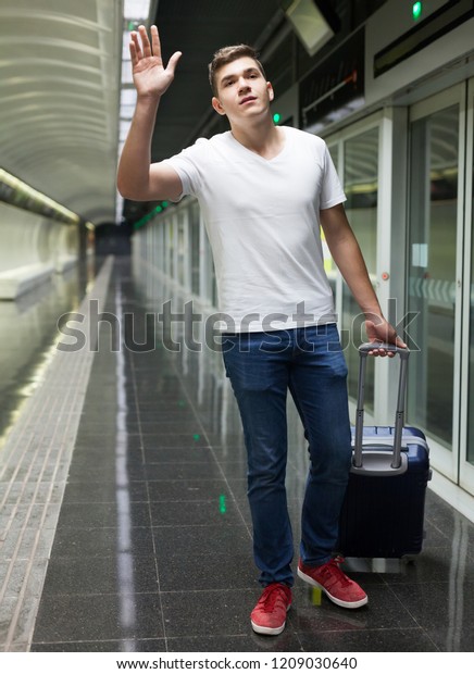 Portrait of young European man with luggage bag\
in subway station