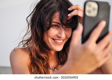 Portrait Of Young European Woman Smiling While Taking A Selfie With Cell Phone On White Background