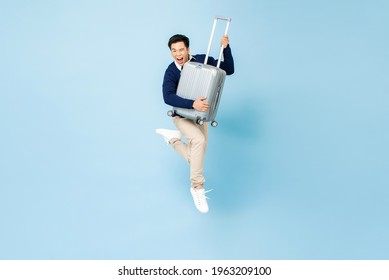 Portrait Of Young Excited Handsome Asian Tourist Man With Baggage Jumping In Mid-air Ready To Travel Isolated On Light Blue Studio Background