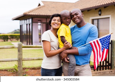 portrait of young family holding american flag outside their house