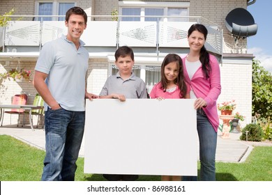 Portrait Of Young Family Holding A Black White Board Outside Their House