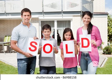 Portrait Of Young Family Holding A Sold Sign In Front Of Their Home