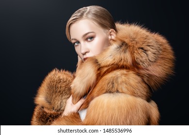 A portrait of a young fashionable woman in a fur coat with a hood. Beauty, fashion.
