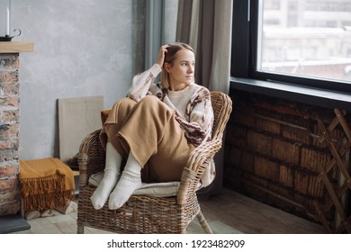 Portrait of young fashionable  woman sitting in wicker armchair near fireplace in stylish vacation home.