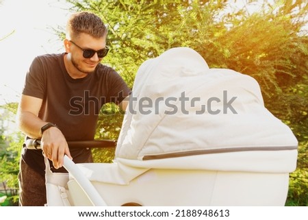 Portrait of a young father while walking with a child in a stroller. A man walks with a baby in a stroller around the city. High quality photo