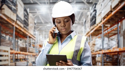 Portrait of young female African American engineer in helmet speaking on smartphone using tablet device standing at construction site. Woman wearing safety equipment at work. Construction concept. - Powered by Shutterstock