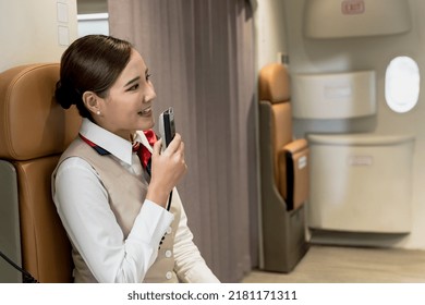 Portrait Young Female Asian Cabin Crew Using Announcing Phone On Board, Woman Flight Attendant Holding Microphone To Annouce Welcome On Board, Female Air Hostess Greeting Passengers On Plane