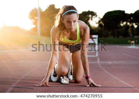 Portrait of young female athlete launching off the start line in a race.