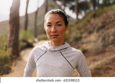 Portrait Of Young Female Athlete Standing Outdoors And Looking At Camera. Woman Runner Outdoors On Country Road Taking A Break After Running Exercise.