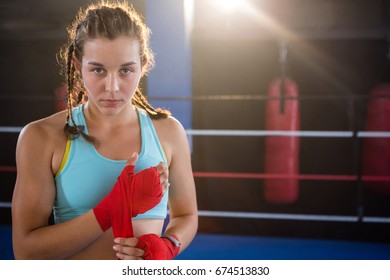 Portrait of young female athlete wrapping red bandage on hand in boxing ring at fitness studio - Powered by Shutterstock