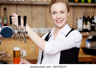 Portrait Of Young Female Bartender Filling Beer In Glass At Restaurant