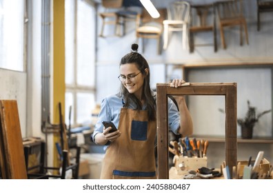 Portrait of young female carpenter using mobile phone in her workshop - Powered by Shutterstock