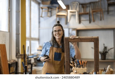 Portrait of young female carpenter using mobile phone in her workshop - Powered by Shutterstock