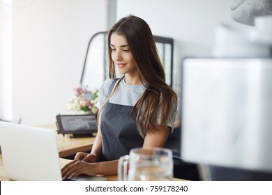 Portrait Of Young Female Coffee Shop Owner Using A Laptop Waiting For Her First Customer Early In The Morning. Woman Running Her Business.