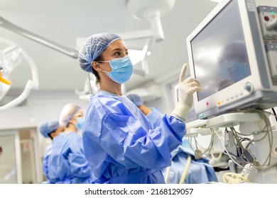 Portrait Of A Young Female Doctor In Scrubs And A Protective Face Mask Preparing An Anesthesia Machine Before An Operation