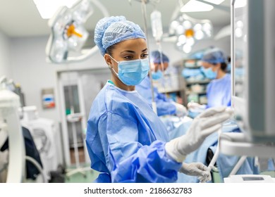 Portrait Of A Young Female Doctor In Scrubs And A Protective Face Mask Preparing An Anesthesia Machine Before An Operation