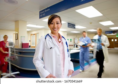Portrait of young female doctor standing in busy hospital ward