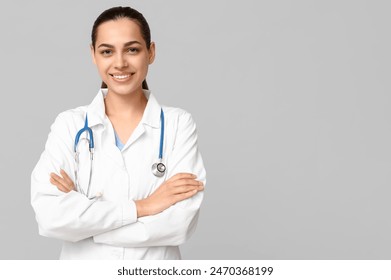 Portrait of young female doctor with stethoscope on grey background - Powered by Shutterstock