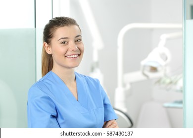 Portrait of a young female doctor wearing a blue coat posing in a dentist office with medical equipment in the background