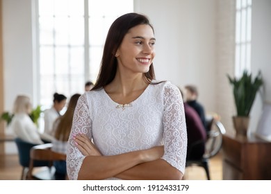 Portrait Of Young Female Employee In Casual Wear Poses For Camera In Modern Office With Colleagues On Background. Happy Student Looking Away, Dreaming, Smiling. Corporate Business Picture Concept