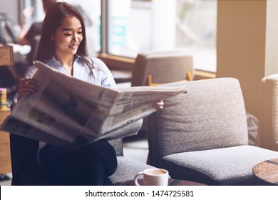 Portrait of a young female freelancer sitting in the cafe, holding a newspaper, and reading it. Horizontal shot - Powered by Shutterstock