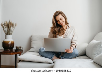 Portrait of a young female freelancer sitting on the couch and using laptop at home happily. High quality photo