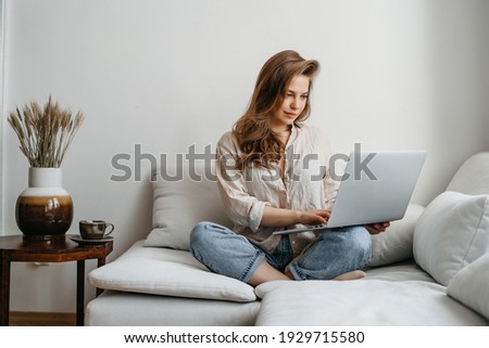 Portrait of a young female freelancer sitting on the couch and working on project, watching movie on laptop, studying, blogging, resting and chatting online.