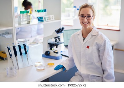 Portrait of a young female lab technician smiling while sitting at a table analyzing samples with a microscope - Shutterstock ID 1932572972
