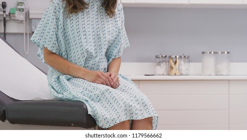 Portrait Of Young Female Patient Seated On Clinic Chair Wearing Hospital Gown