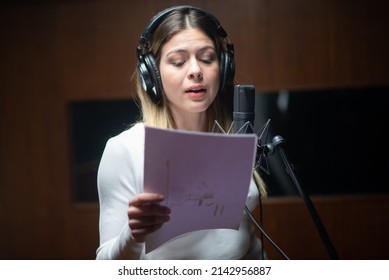 Portrait of young female performer recording song in studio. Caucasian woman holding text and singing song on radio or at sound recording studio. Creating music concept