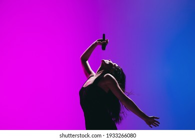 Portrait of young female singer isolated on blue-pink background.