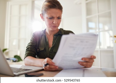 Portrait Of Young Female Sitting At Table Reading Documents. Woman Busy Working At Home Office.