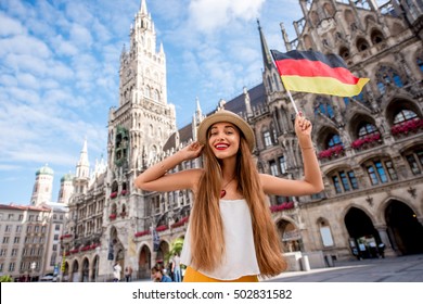 Portrait of a young female tourist with german flag standing on the central square in front of the town hall building in Munich. Having a great vacation in Germany