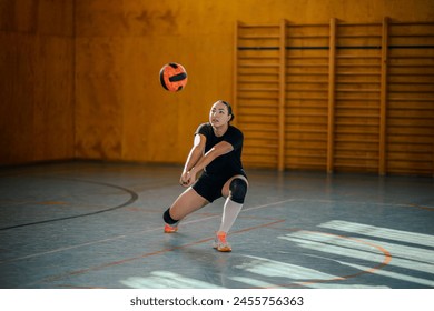 Portrait of a young female volleyball player libero of a volleyball team bumping a ball and practicing volleyball at indoor court. High school volleyball training or a match. Copy space. - Powered by Shutterstock