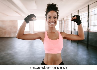 Portrait of young fitness woman flexing muscles and smiling. African female model in sportswear showing her muscles.