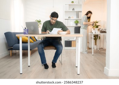 Portrait of a young freelancer smiling while working online via laptop at home with his girlfriend