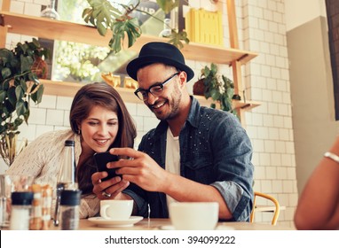 Portrait of young friends sitting in cafe looking at the photos on mobile phone. Happy young people meeting in a restaurant using cell phone. - Powered by Shutterstock