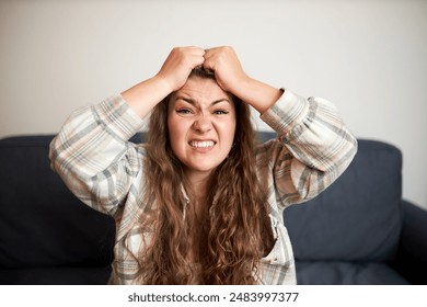 Portrait of young frustrated angry disappointed woman pulling her hair after her favorite team lost at championship, sitting on couch at home and watching live broadcast of football match - Powered by Shutterstock